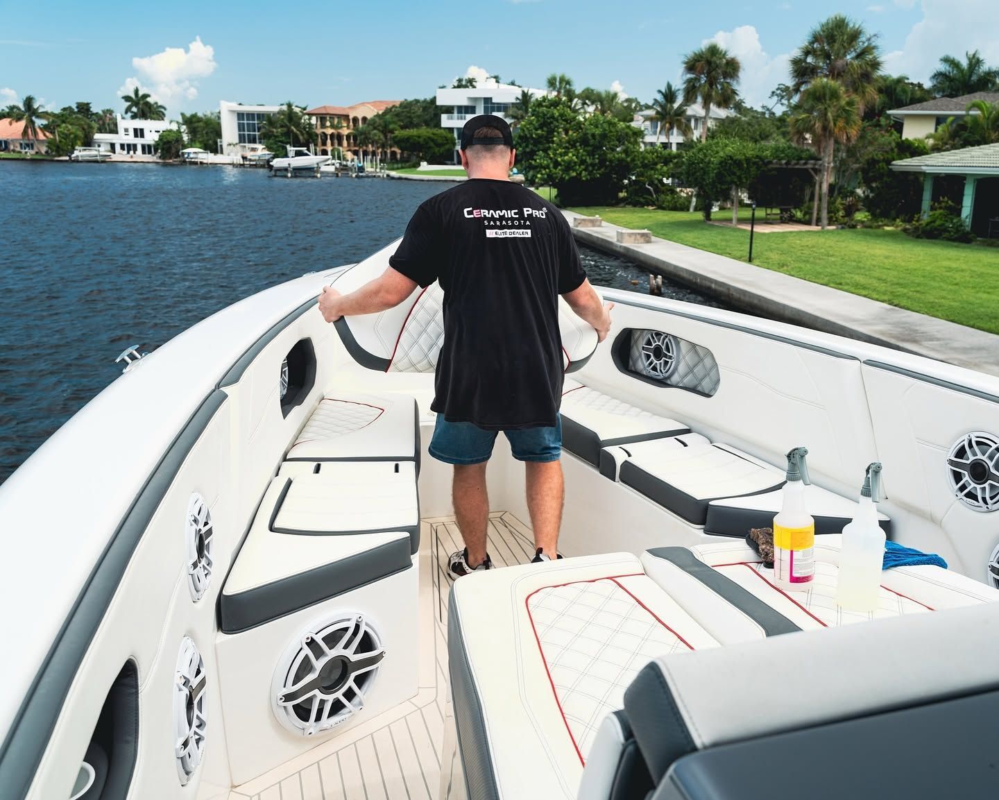 Person standing on a white boat deck on a calm canal, facing the water and waterfront homes.