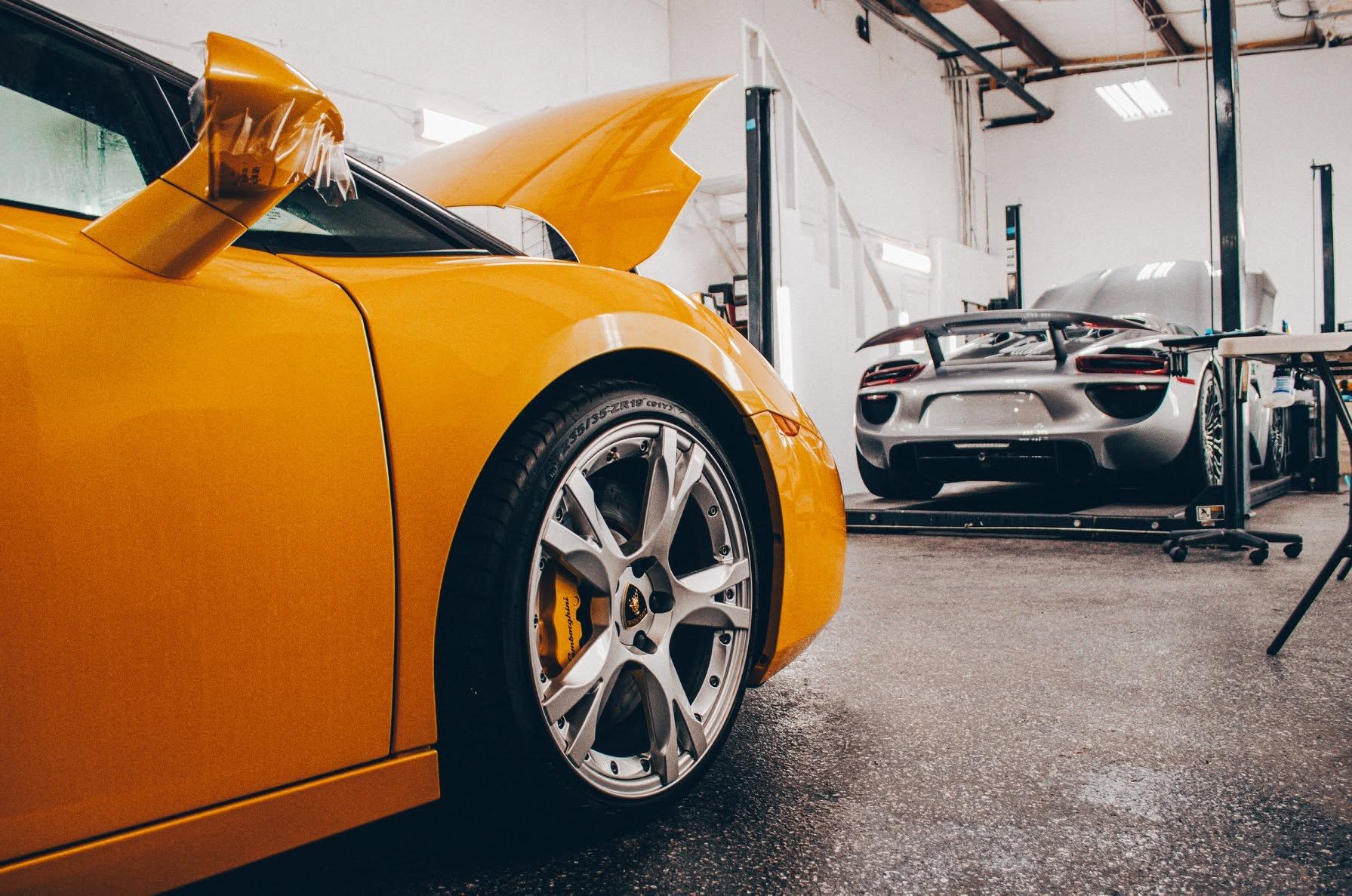 Orange sports car in a garage, with a white supercar in the background