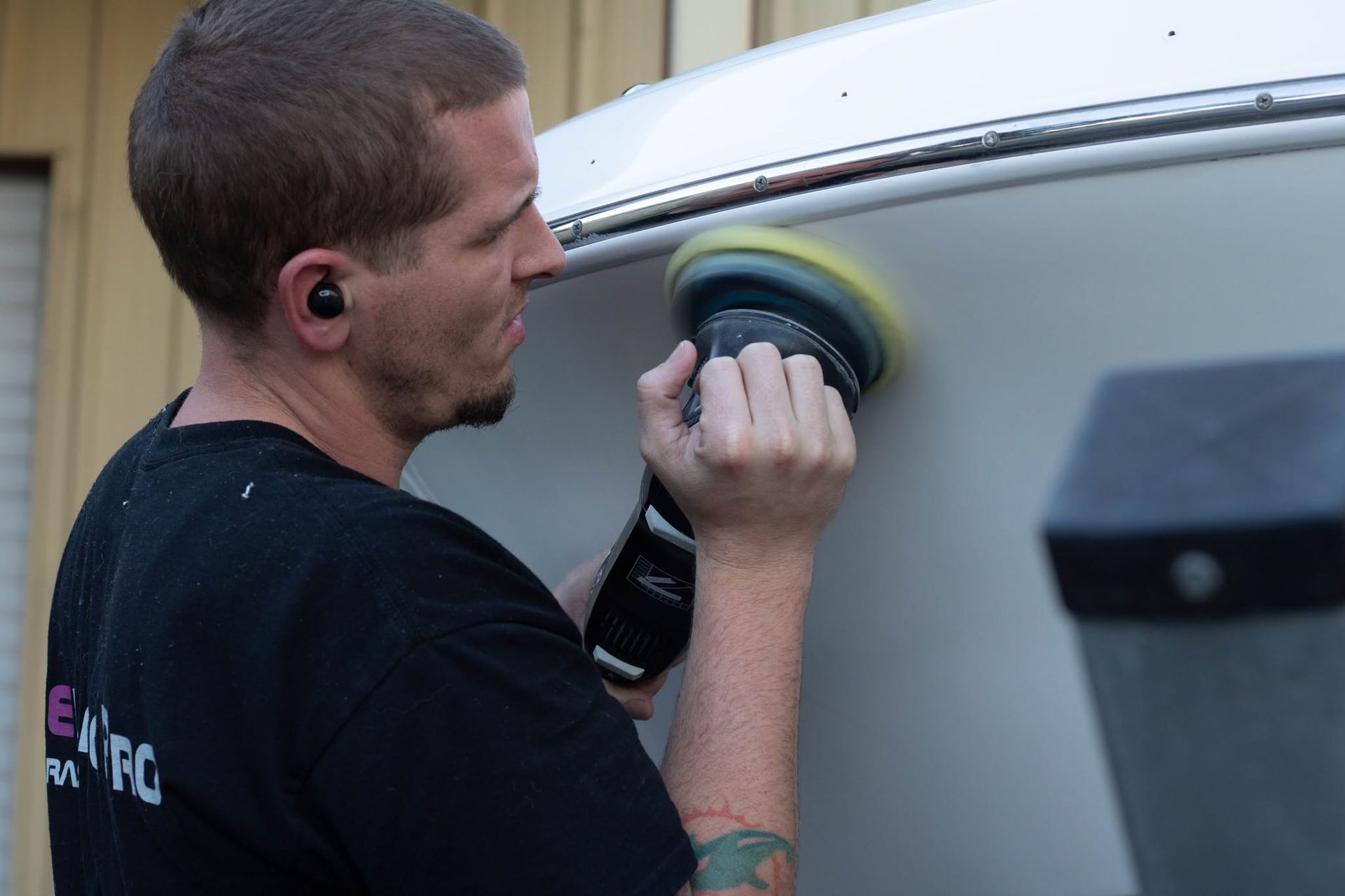 Man polishing a white vehicle with a buffer, standing beside the side panel outdoors
