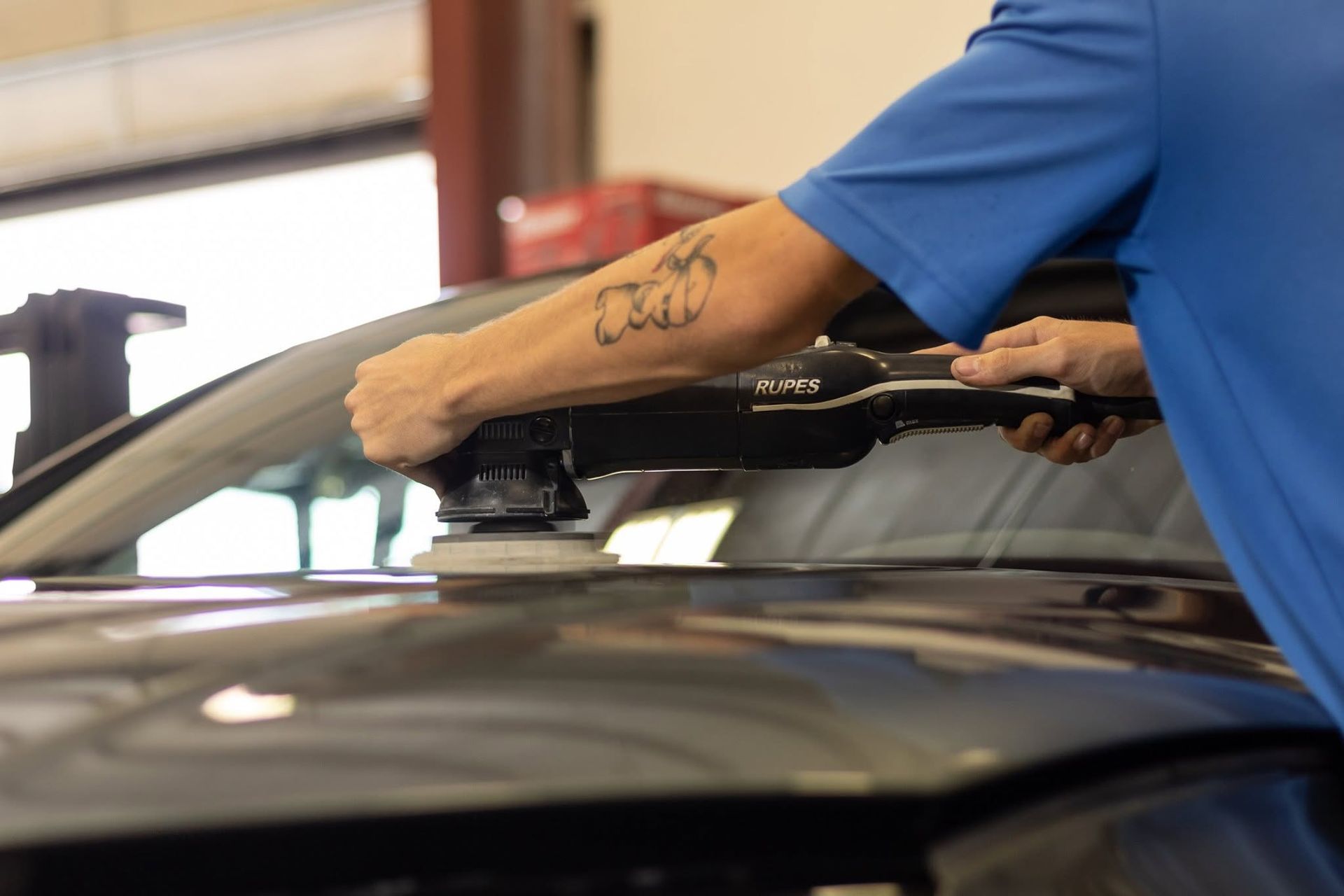 Person using a polisher on a car hood in an auto shop