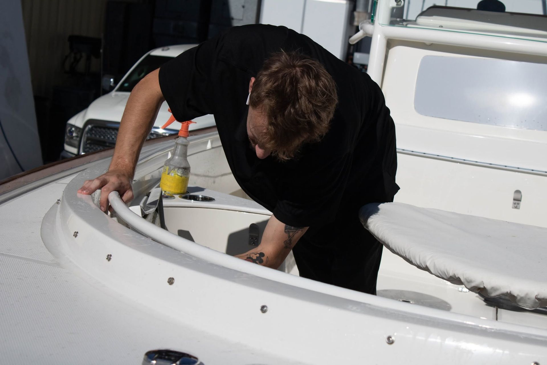 Person leaning into a white boat compartment, working with tools near a yellow bottle.