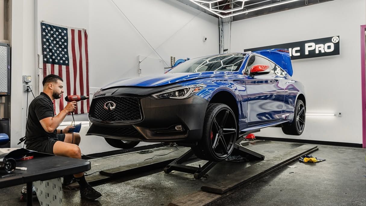 Blue car on a dynamometer in a workshop, with a technician working beside it.