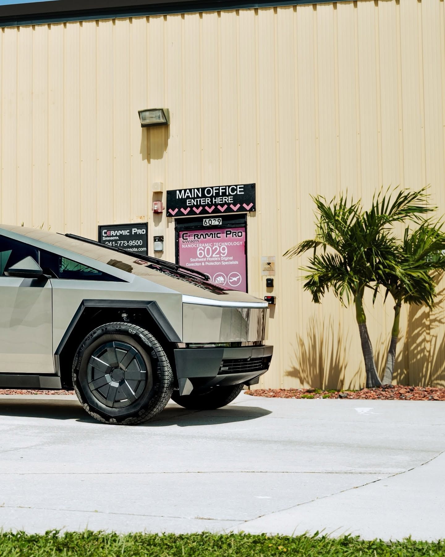 Cybertruck parked by a beige building with a pink sign and palm plant
