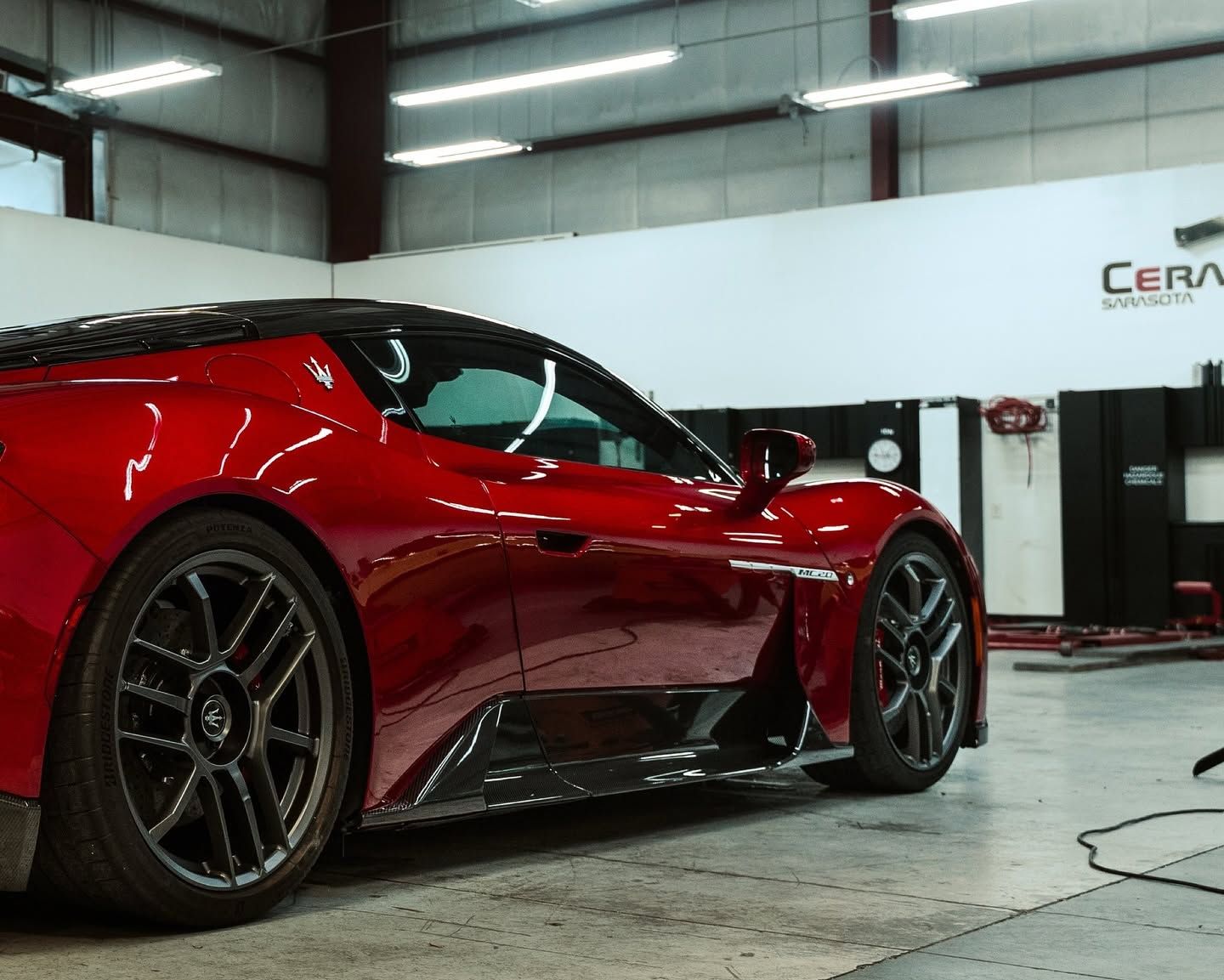 Red sports car in a garage, shown from the side with glossy black wheels.