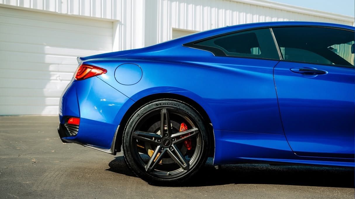 Blue sports coupe parked outdoors, side view with black wheels and red brake calipers.