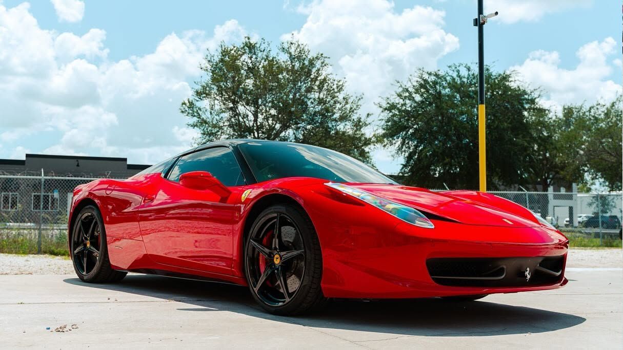 Red sports car parked outdoors on a sunny day, side view with black wheels and blue sky.