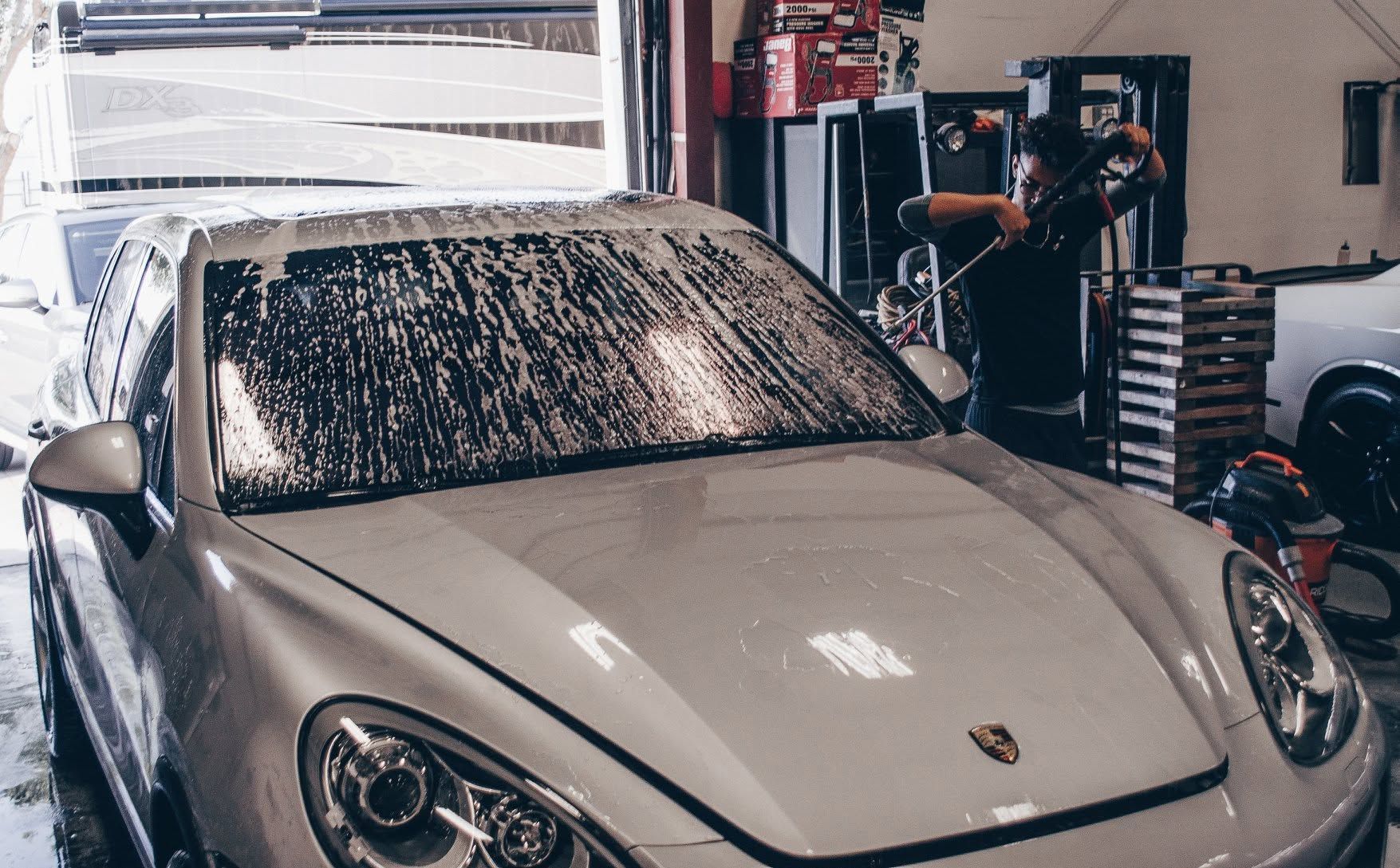 Silver sports car covered in soap suds inside an auto shop