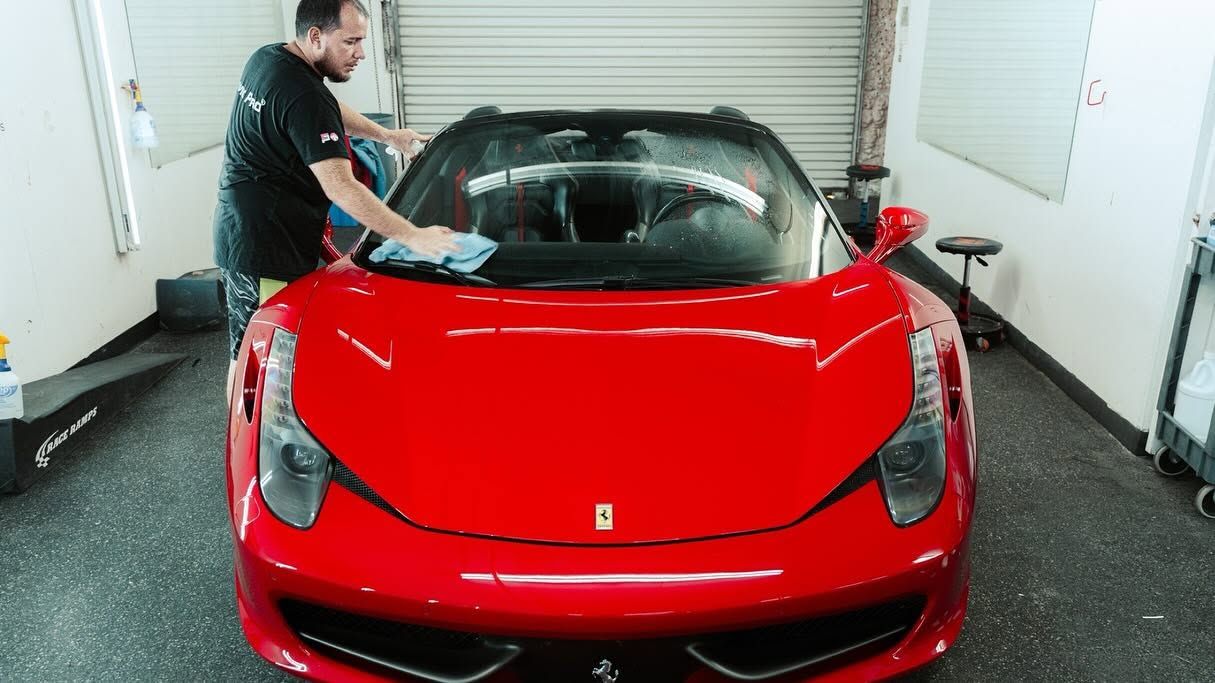 Person washing a red sports car in a garage or car wash bay