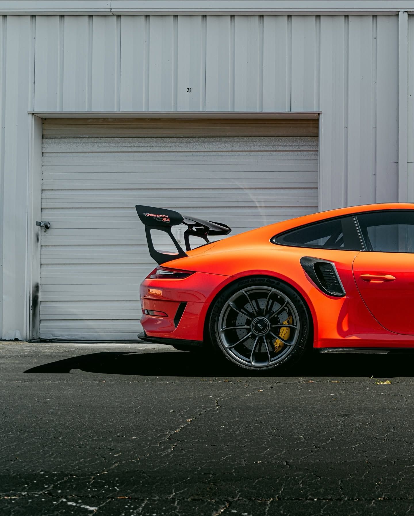 Orange sports car with large rear wing parked in front of a white garage door.