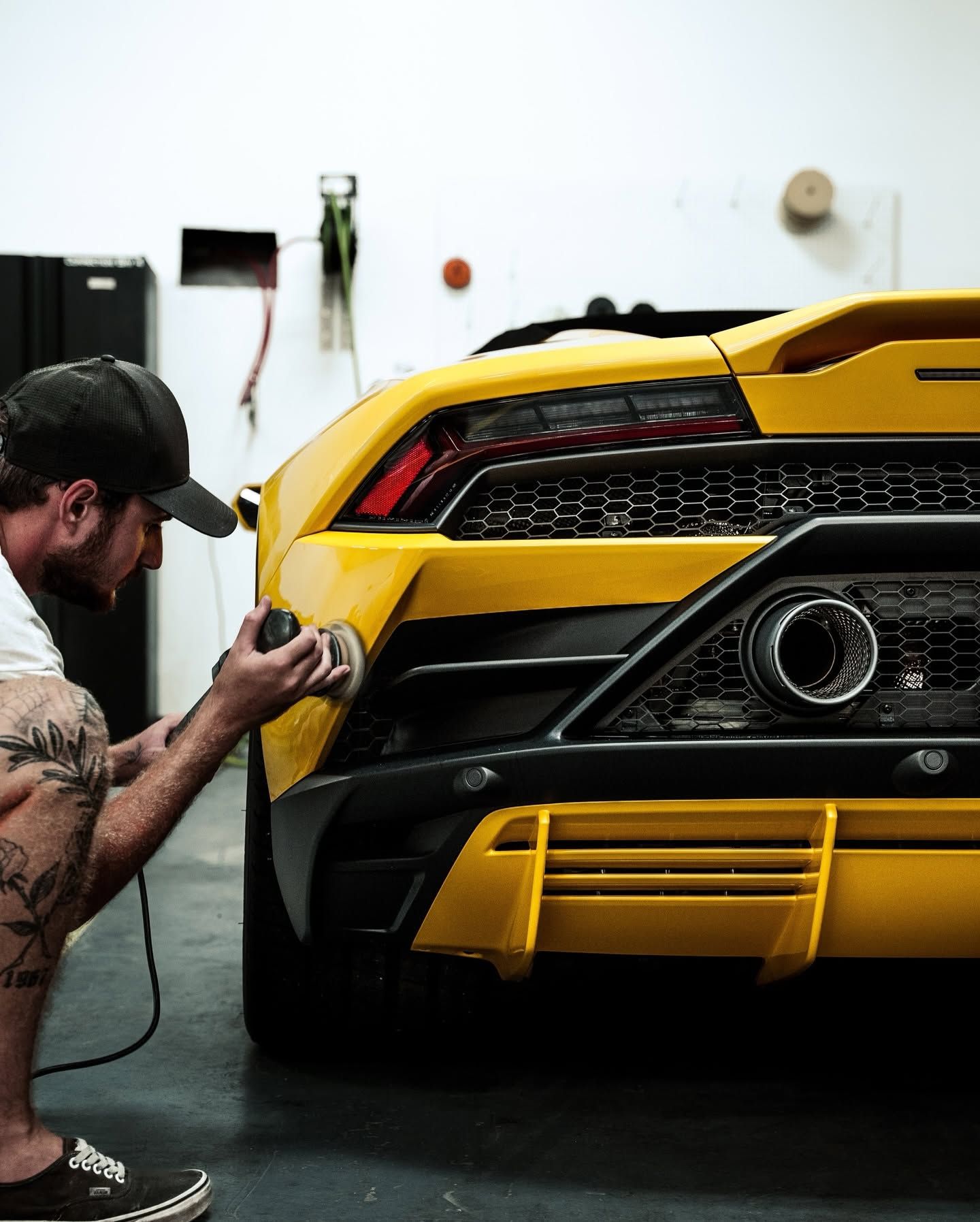 Mechanic polishing yellow sports car rear bumper in a garage