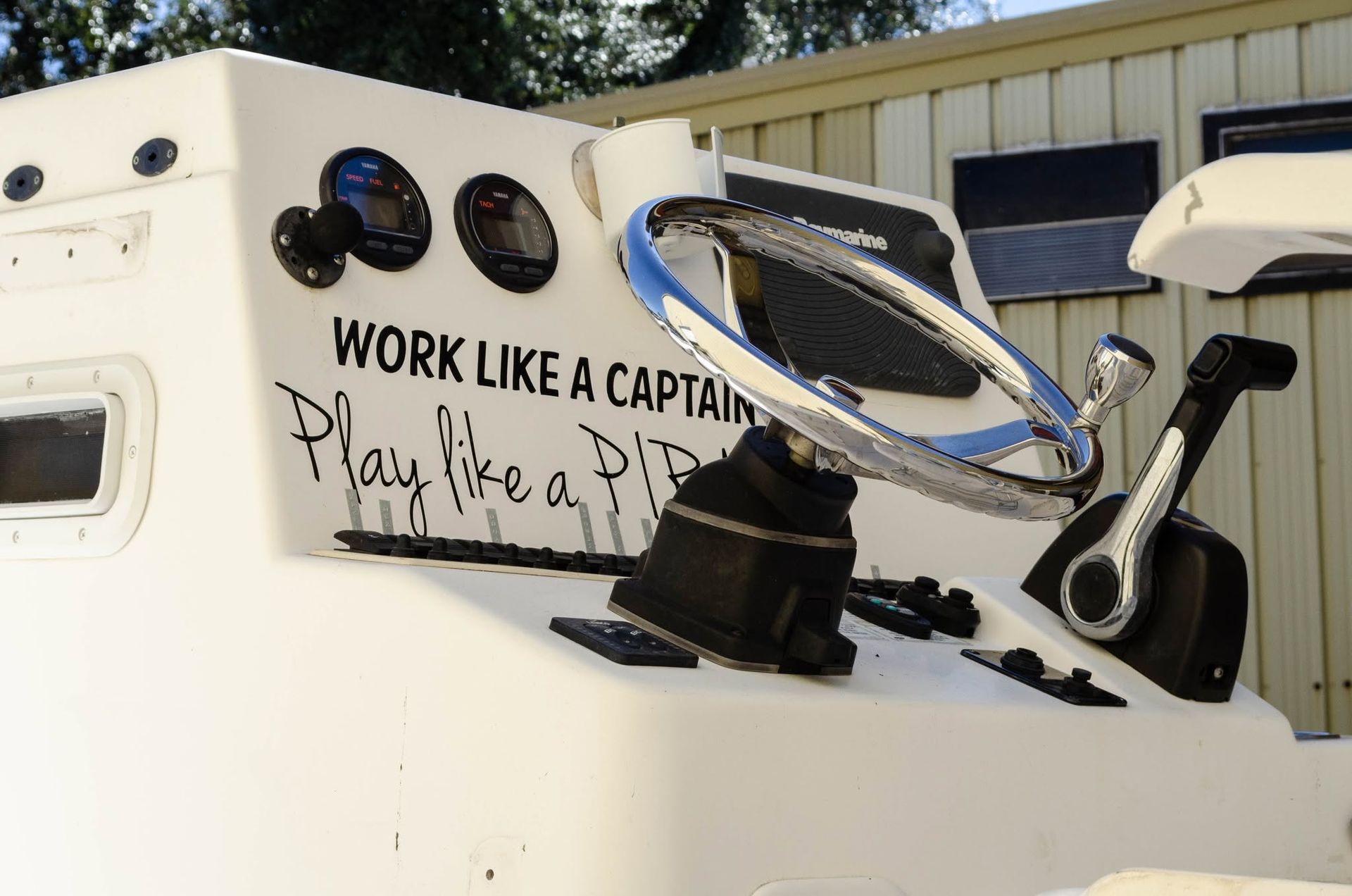 Steering wheel and helm on a boat with “Work like a captain, play like a pirate” text on the cabin side