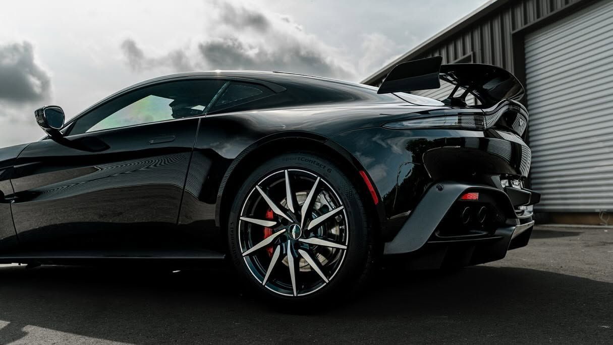 Black sports car parked beside a warehouse, viewed from the front-left in a low-angle shot.
