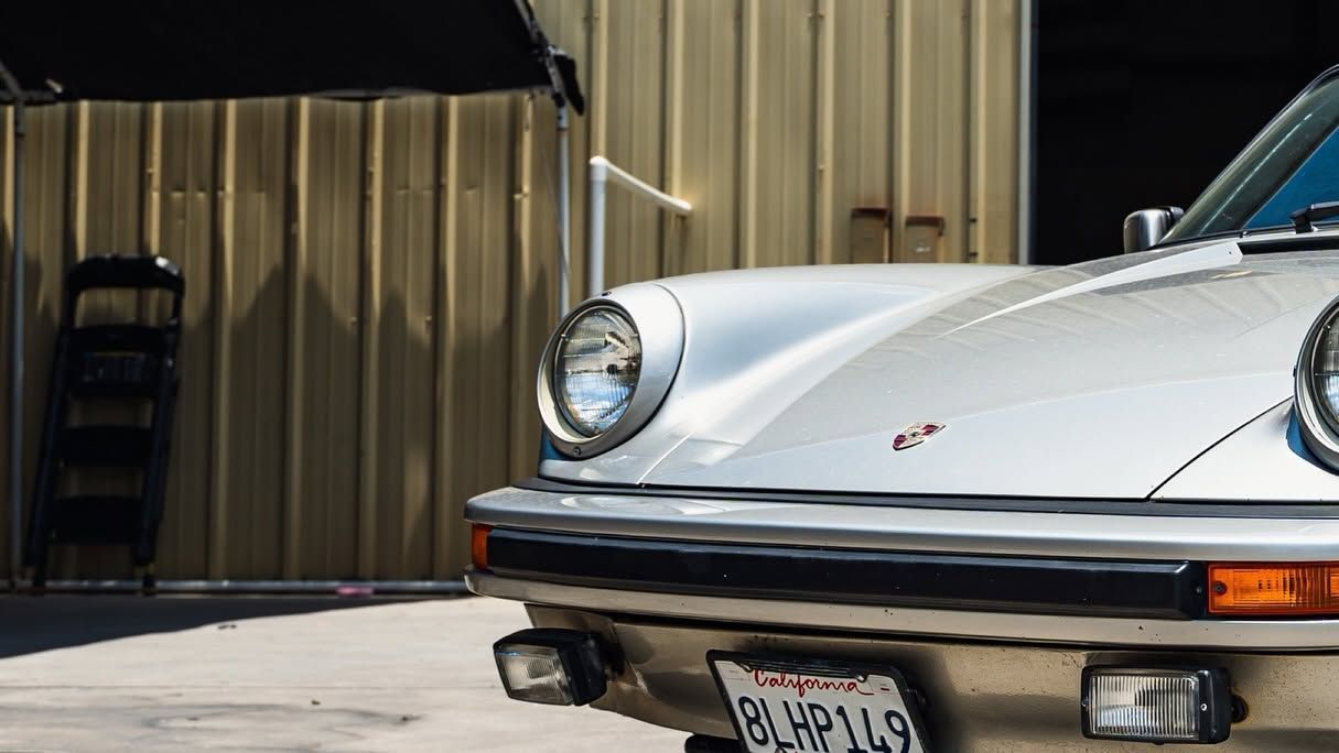 Front of a white classic sports car parked beside a corrugated metal building
