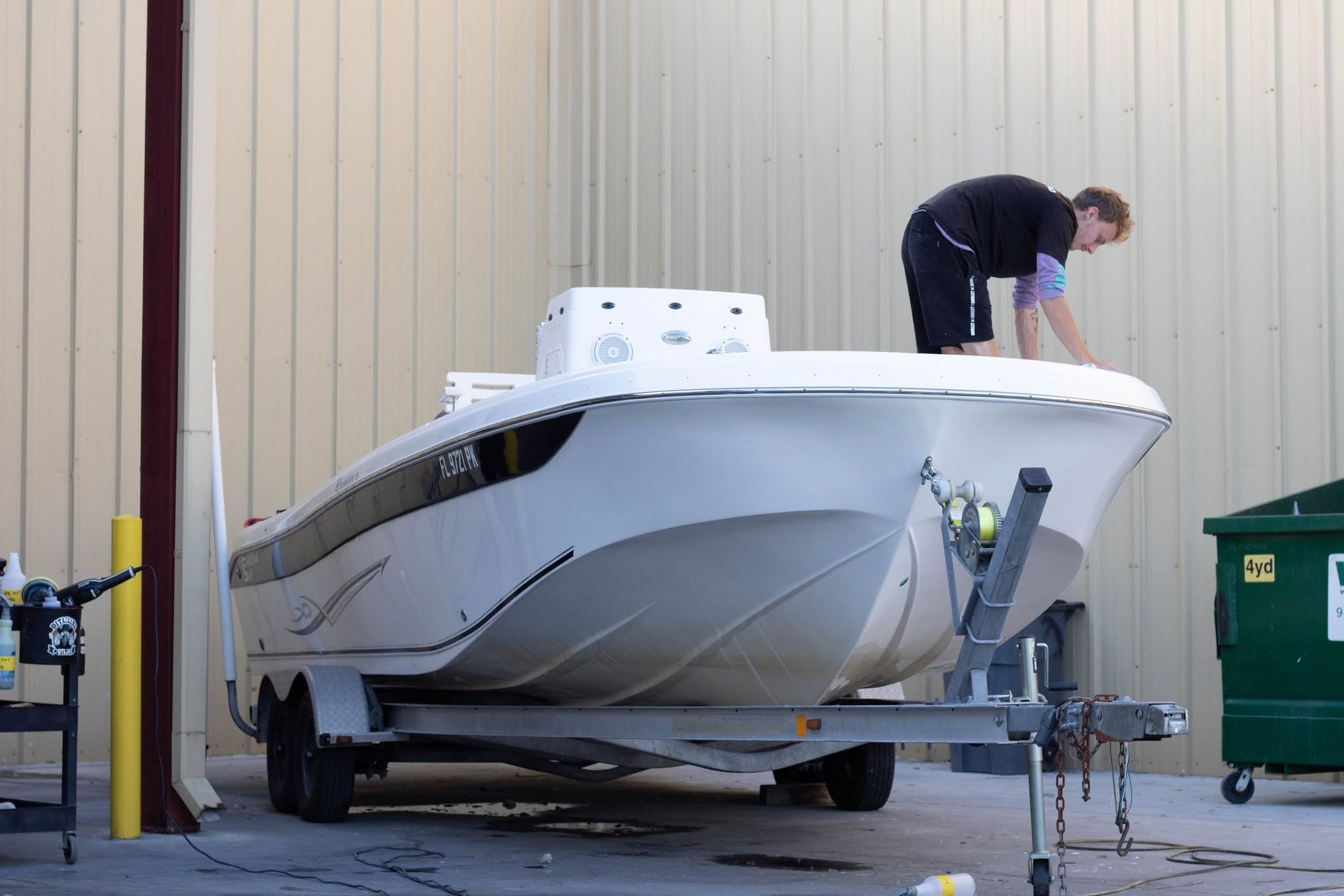 Person cleaning a white boat on a trailer outside a building