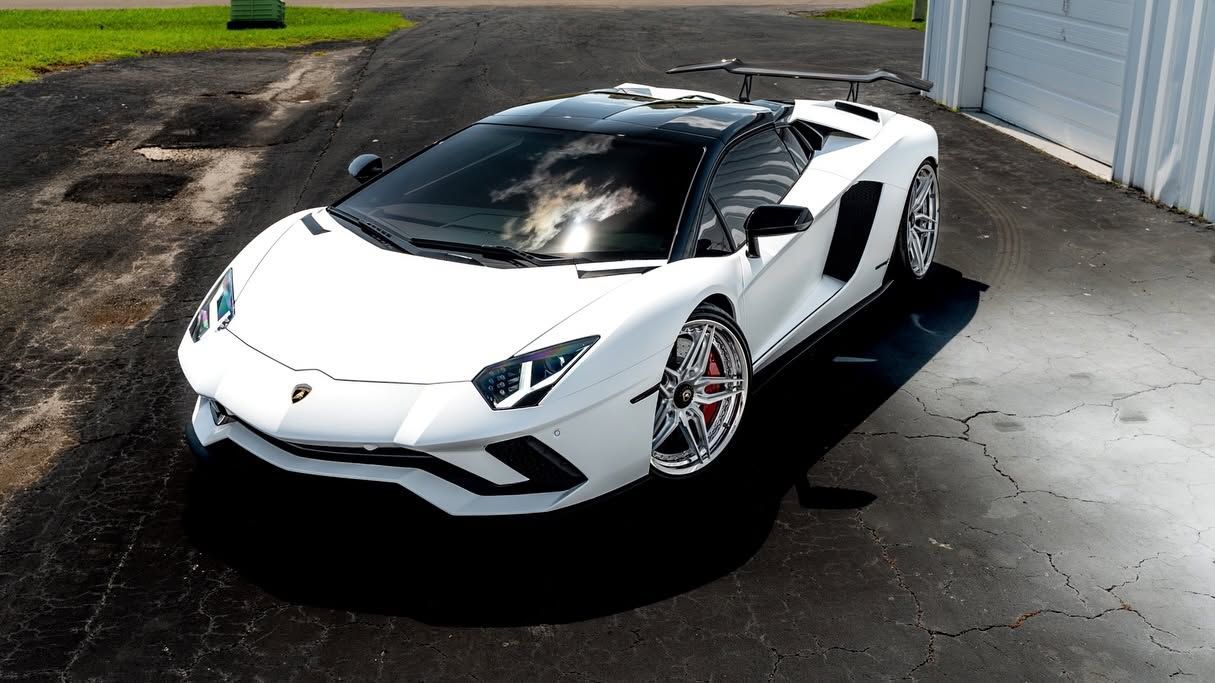 White sports car parked on a driveway beside a garage, viewed from the front-left side.
