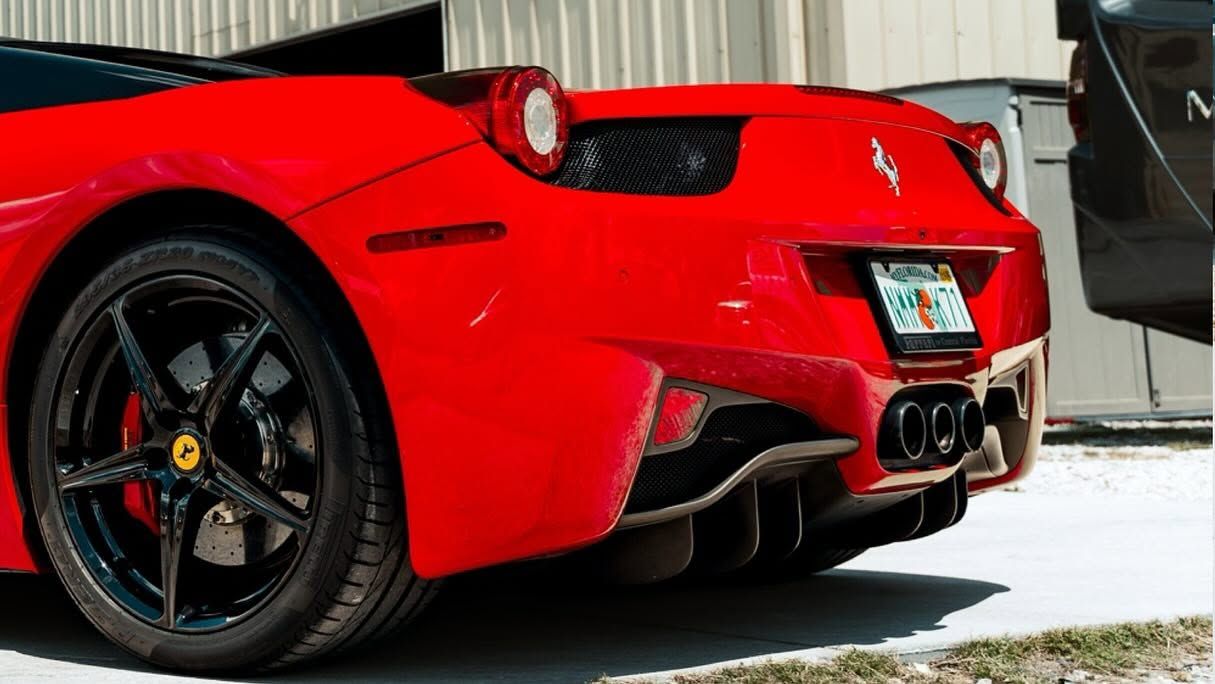 Rear view of a red sports car with black wheels parked outdoors near a building