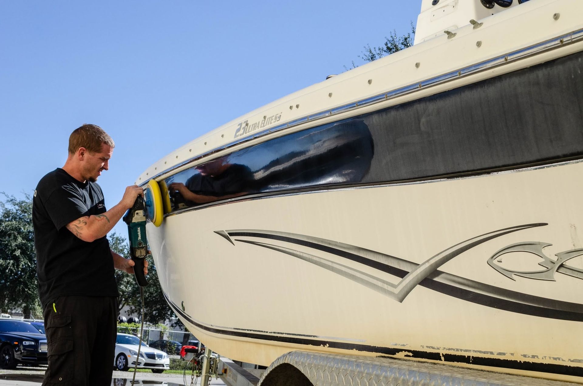 Man polishing the side of a white boat with a cloth outdoors, reflecting sunlight.