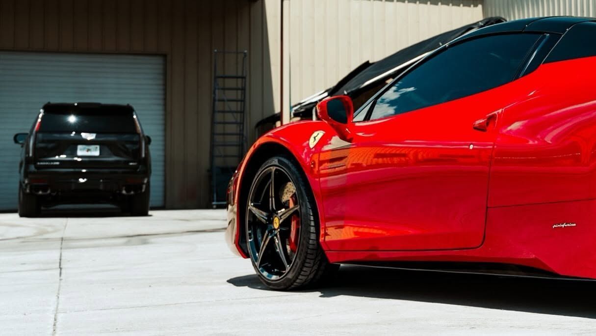 Red sports car parked beside a black SUV in a garage driveway.