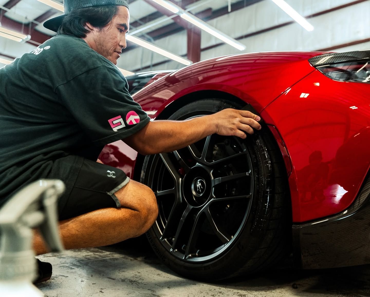 Mechanic kneeling beside a red sports car, inspecting the front wheel in a garage
