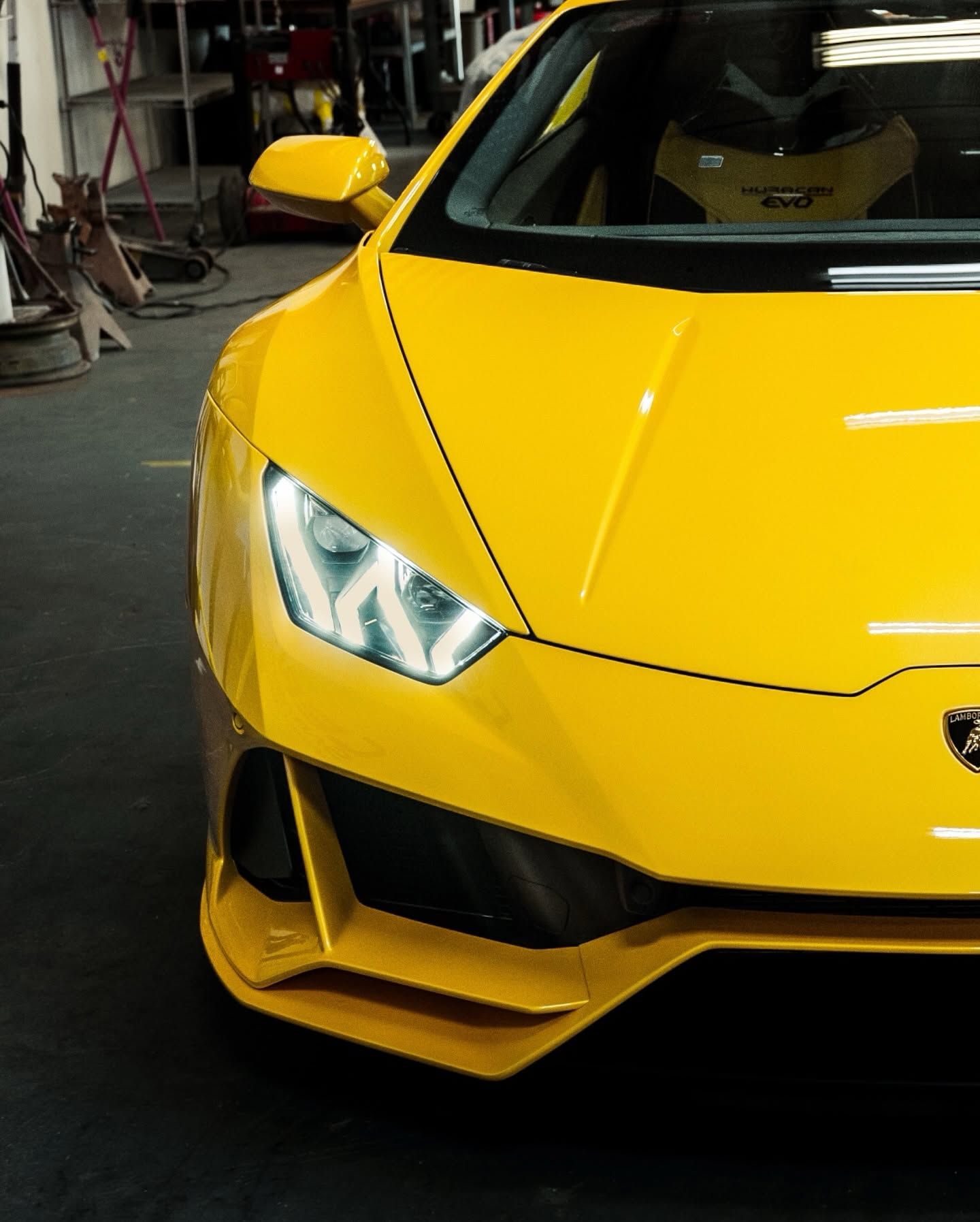 Bright yellow sports car front end in a garage, with sharp headlights and low aerodynamic bumper