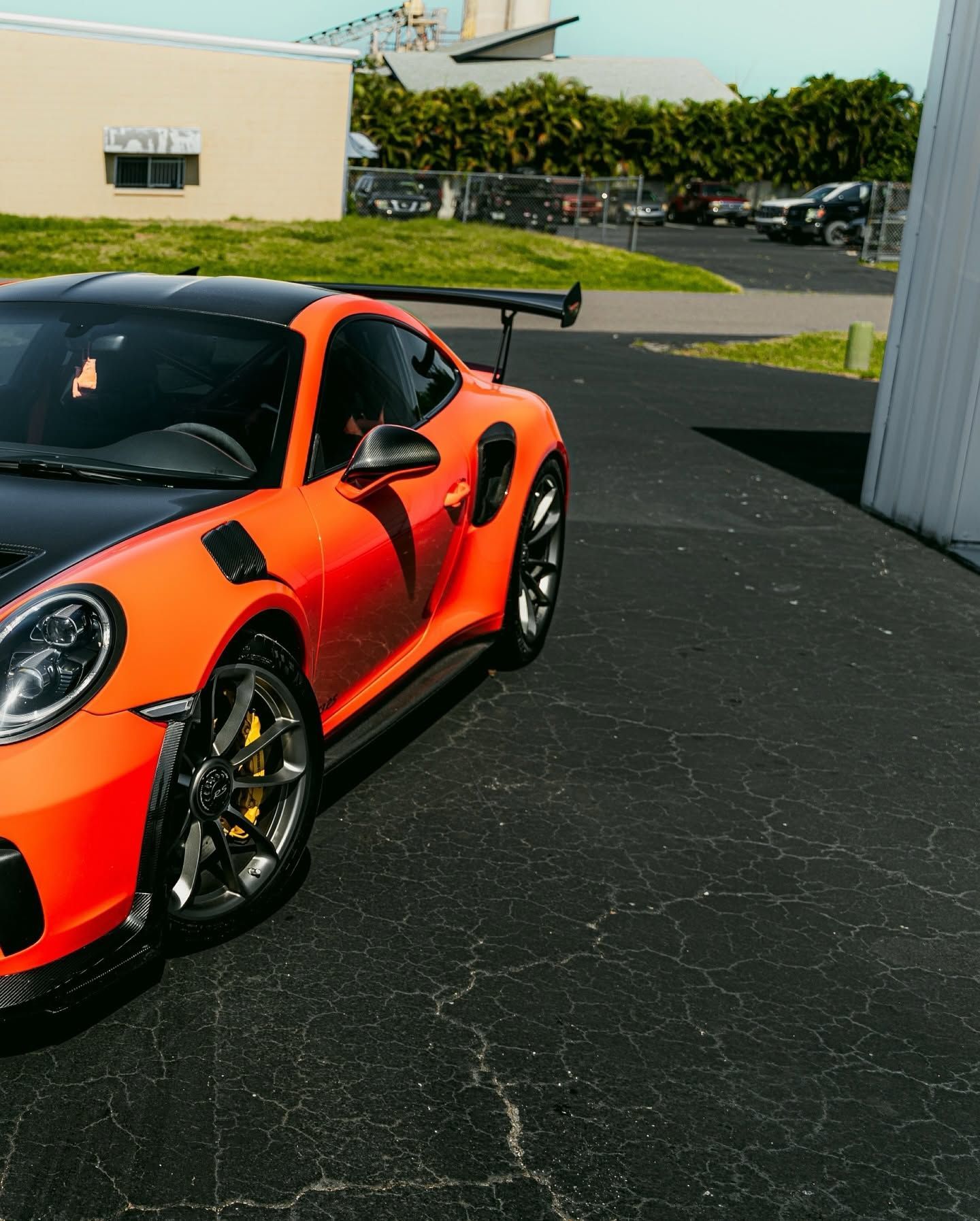Orange sports car parked outdoors on blacktop, front-left view with large rear wing and black rims