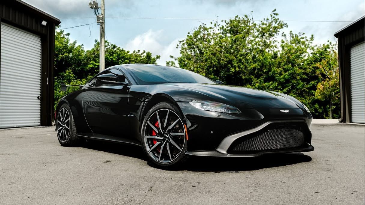 Black sports coupe parked outdoors on a driveway, viewed from the front-left side.