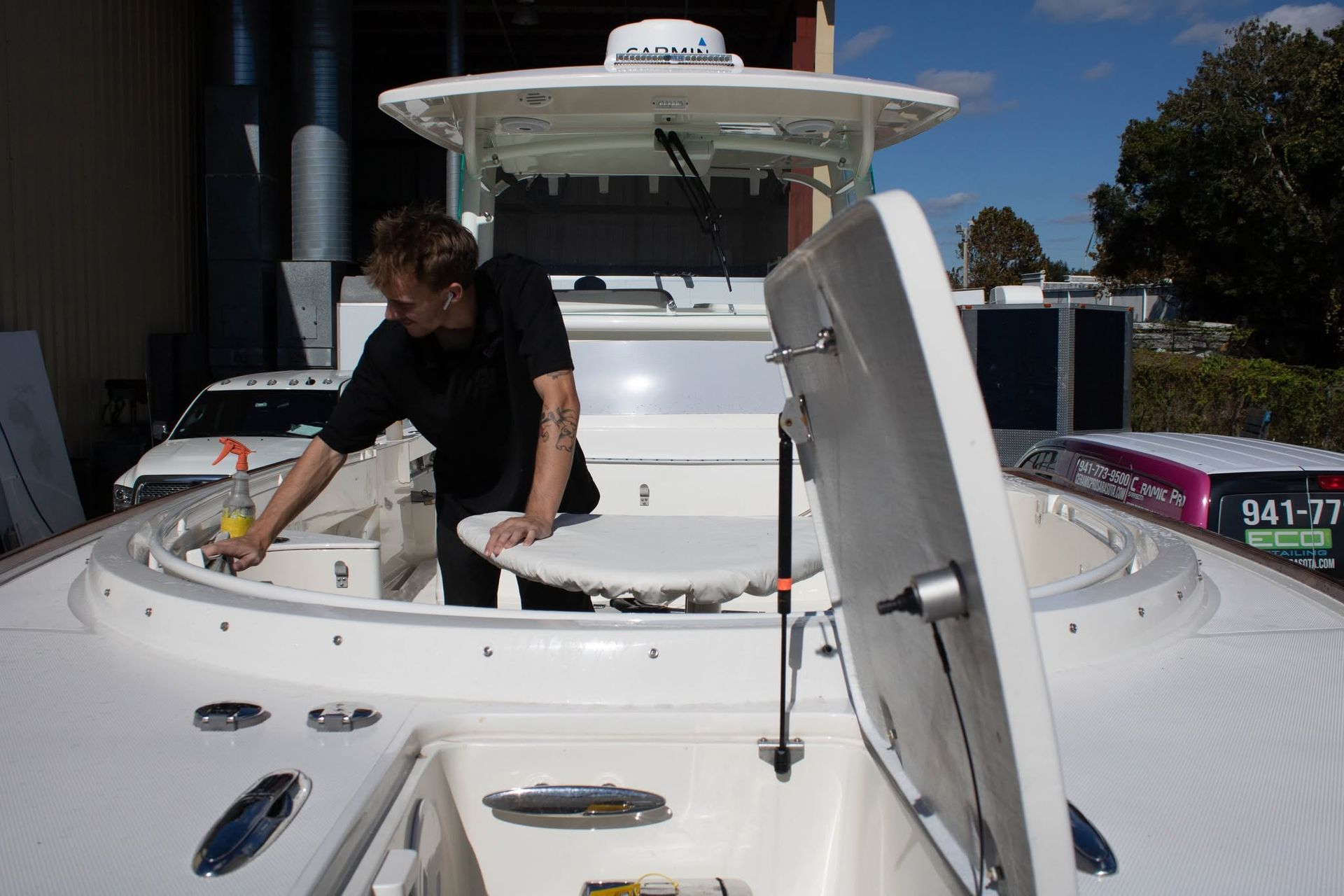 Person cleaning the deck of a white boat in bright sunlight, with an open hatch visible.