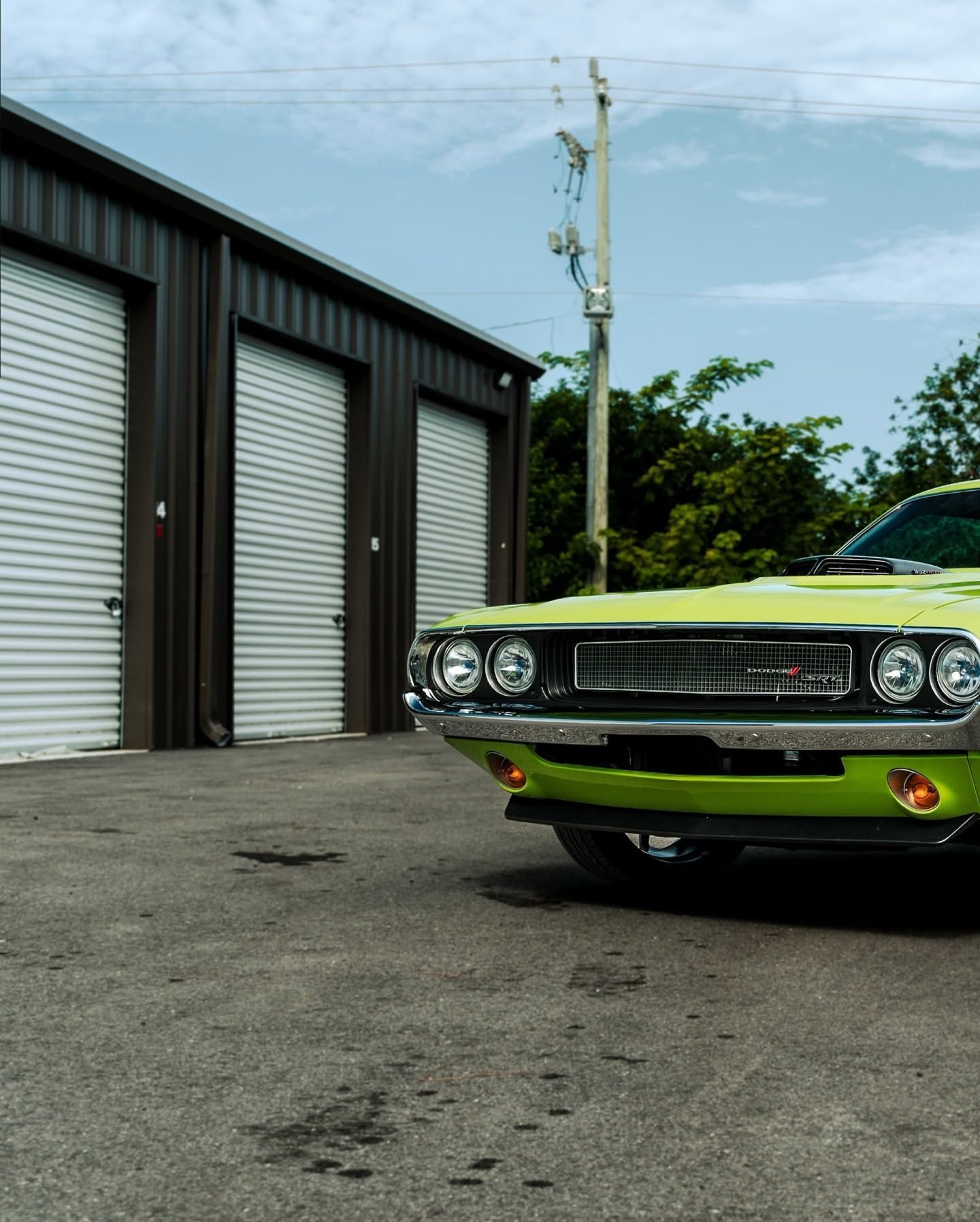 Classic green car parked beside storage units under a cloudy sky.