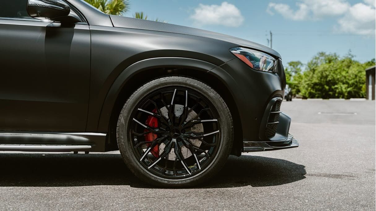 Black sports car close-up with glossy paint and custom black wheel on a sunny road