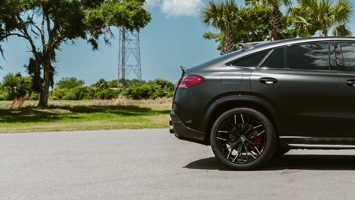 Black SUV driving on a sunny road beside palm trees and greenery.