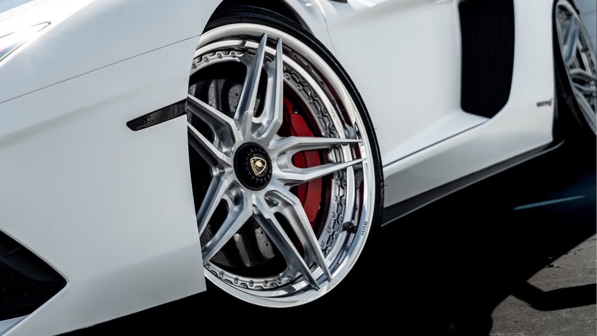 White sports car close-up showing a silver alloy wheel with red brake caliper on a black road