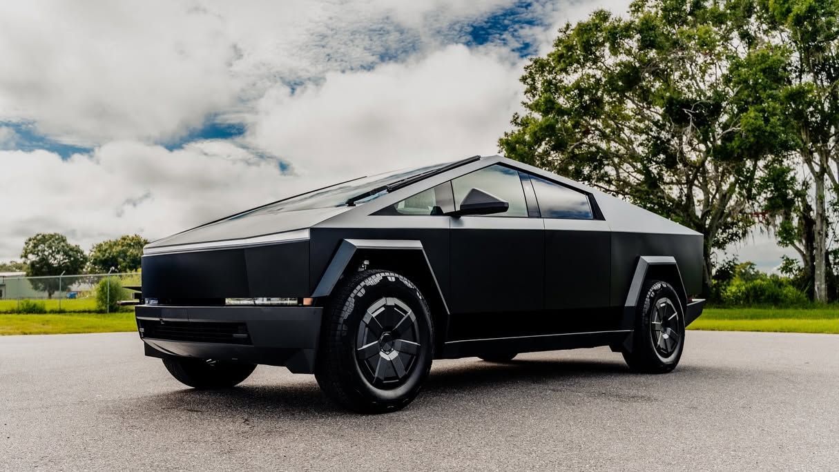 Black Tesla Cybertruck parked on a road with trees and cloudy sky in the background