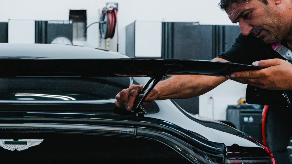 Man polishing a black car in a garage, focusing on the hood with a cloth and tool.