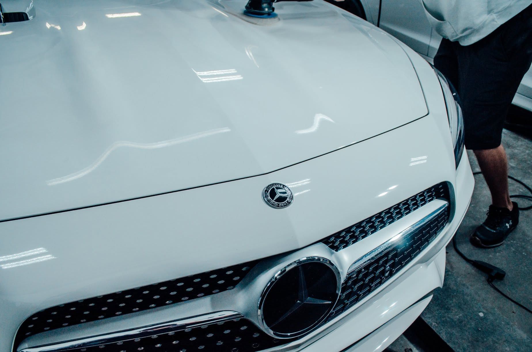 White Mercedes front view in a garage, with a person standing beside it