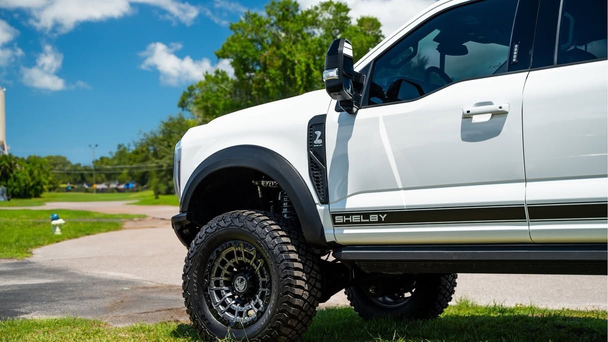 White lifted pickup truck with large off-road tires parked on a sunny street near a grassy park