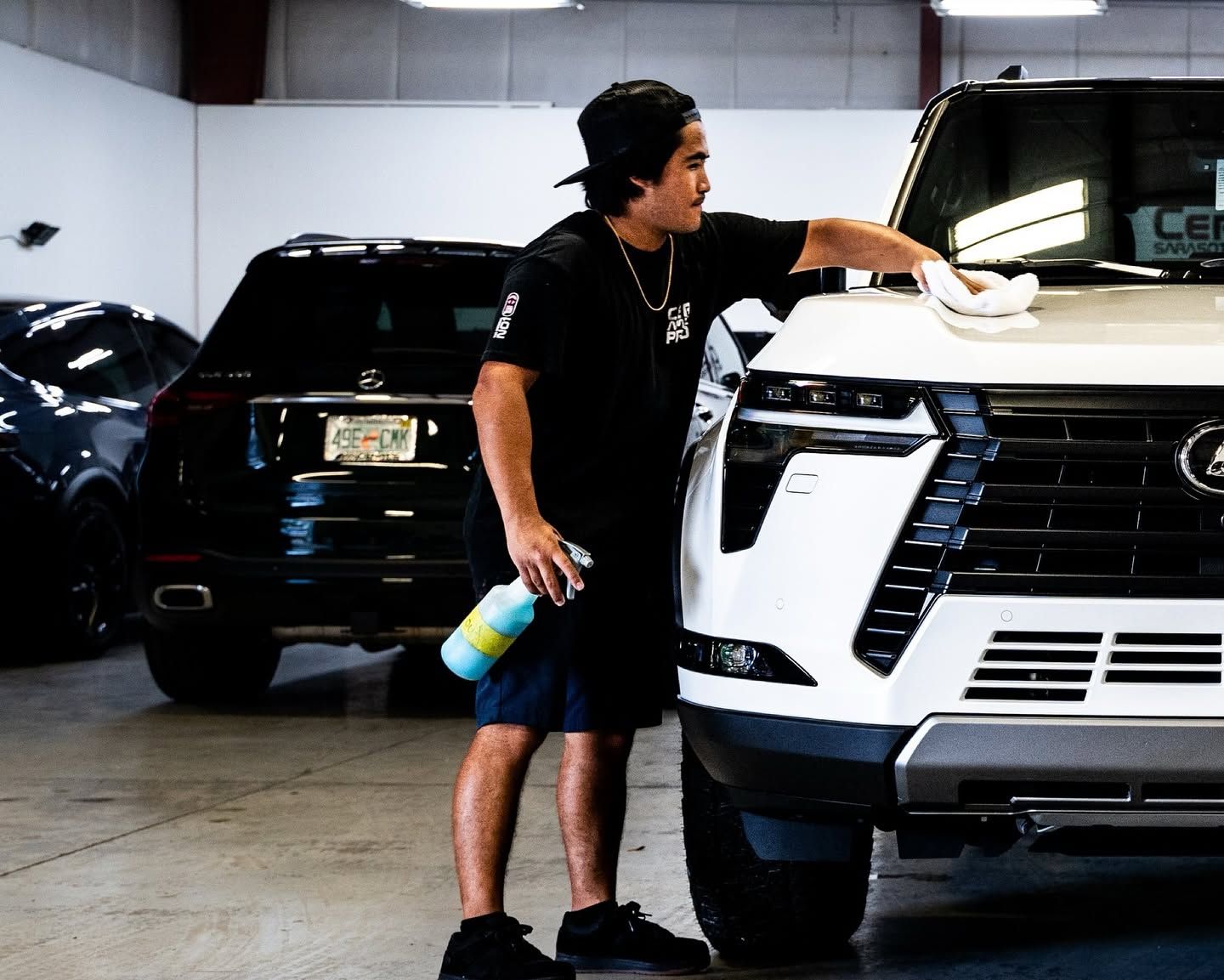 Person washing a white SUV in a garage, with a black SUV parked behind.