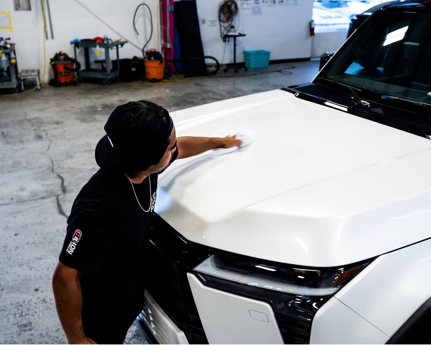 Person wiping the hood of a white car in an auto detailing garage.