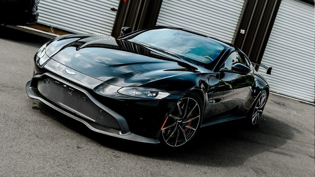 Black sports coupe parked in front of garage doors, viewed from the front-left angle.
