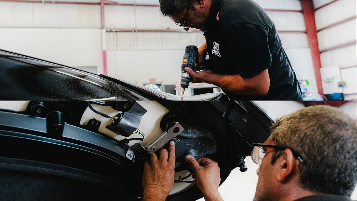 Two people inspect and repair a black motorcycle in a workshop.