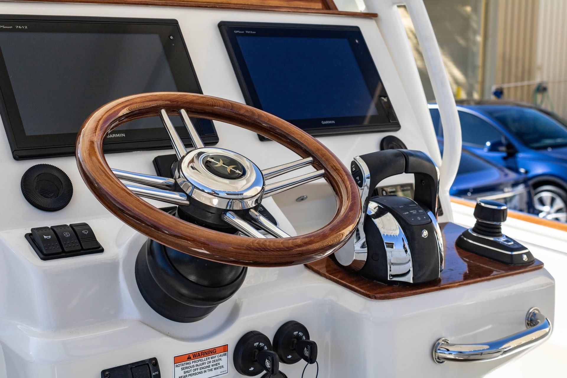 Boat helm with wooden steering wheel, twin displays, and controls on a white dashboard.
