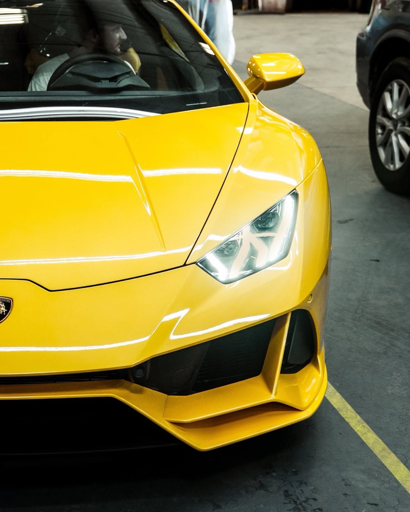 Yellow sports car front end parked in a lot, showing a headlight and black accents