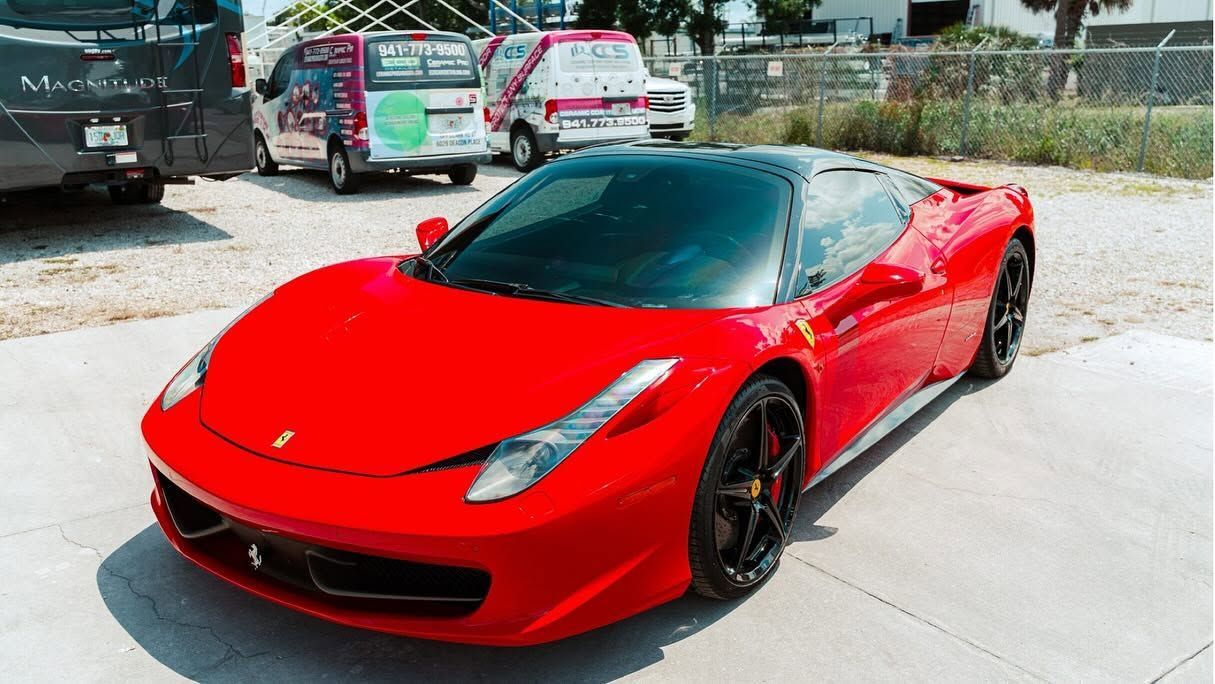Red sports car parked outdoors in a driveway, viewed from the front-left side.