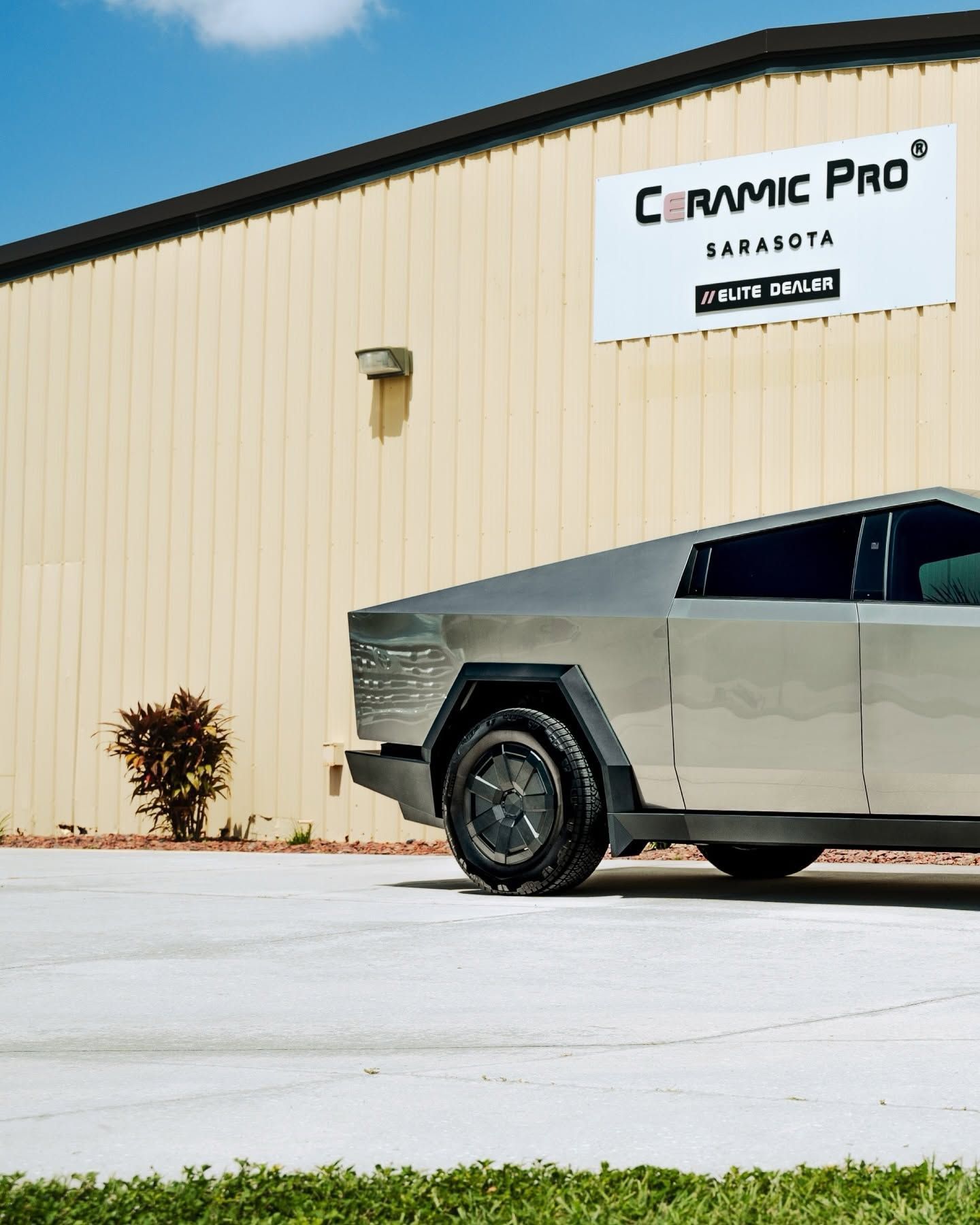 Silver Tesla Cybertruck parked beside a beige building with a Ceramic Pro sign.