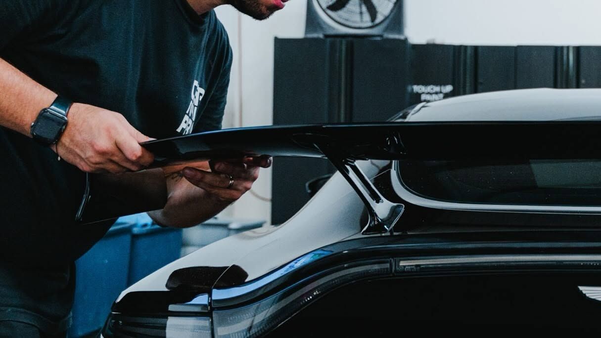 Person adjusting a black car spoiler in a garage workshop