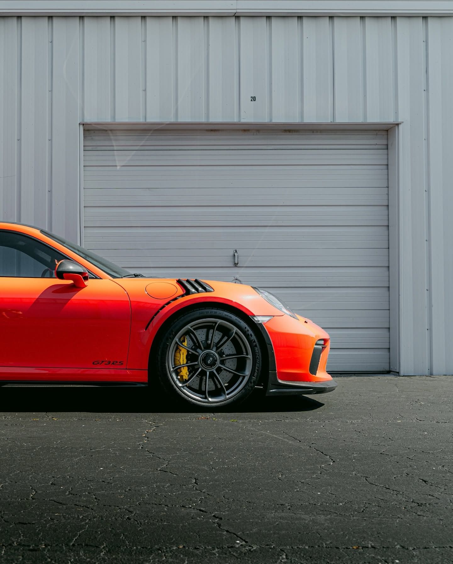 Red sports car parked beside a gray industrial garage door on asphalt.