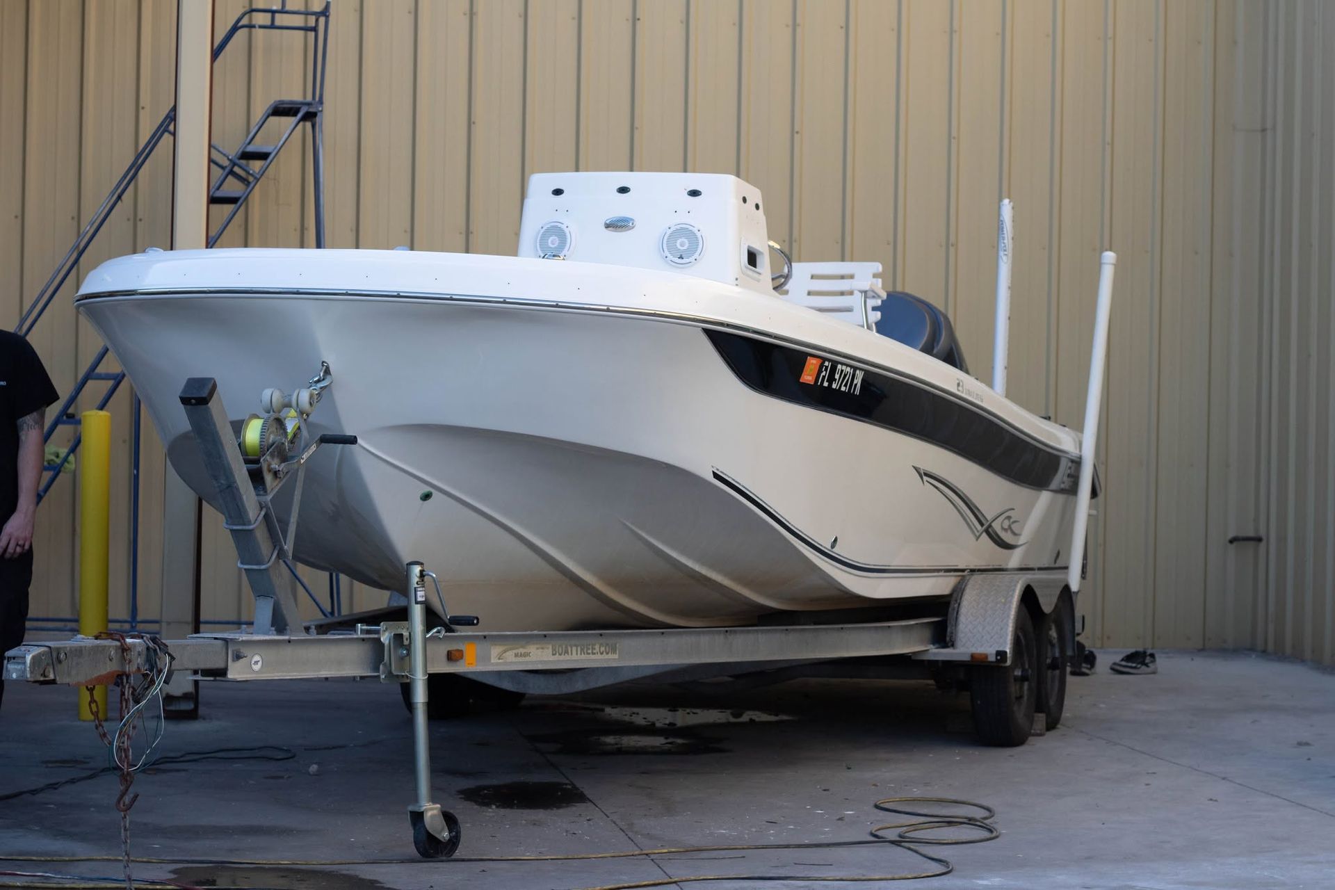 White and black boat on a trailer parked beside a beige metal building.