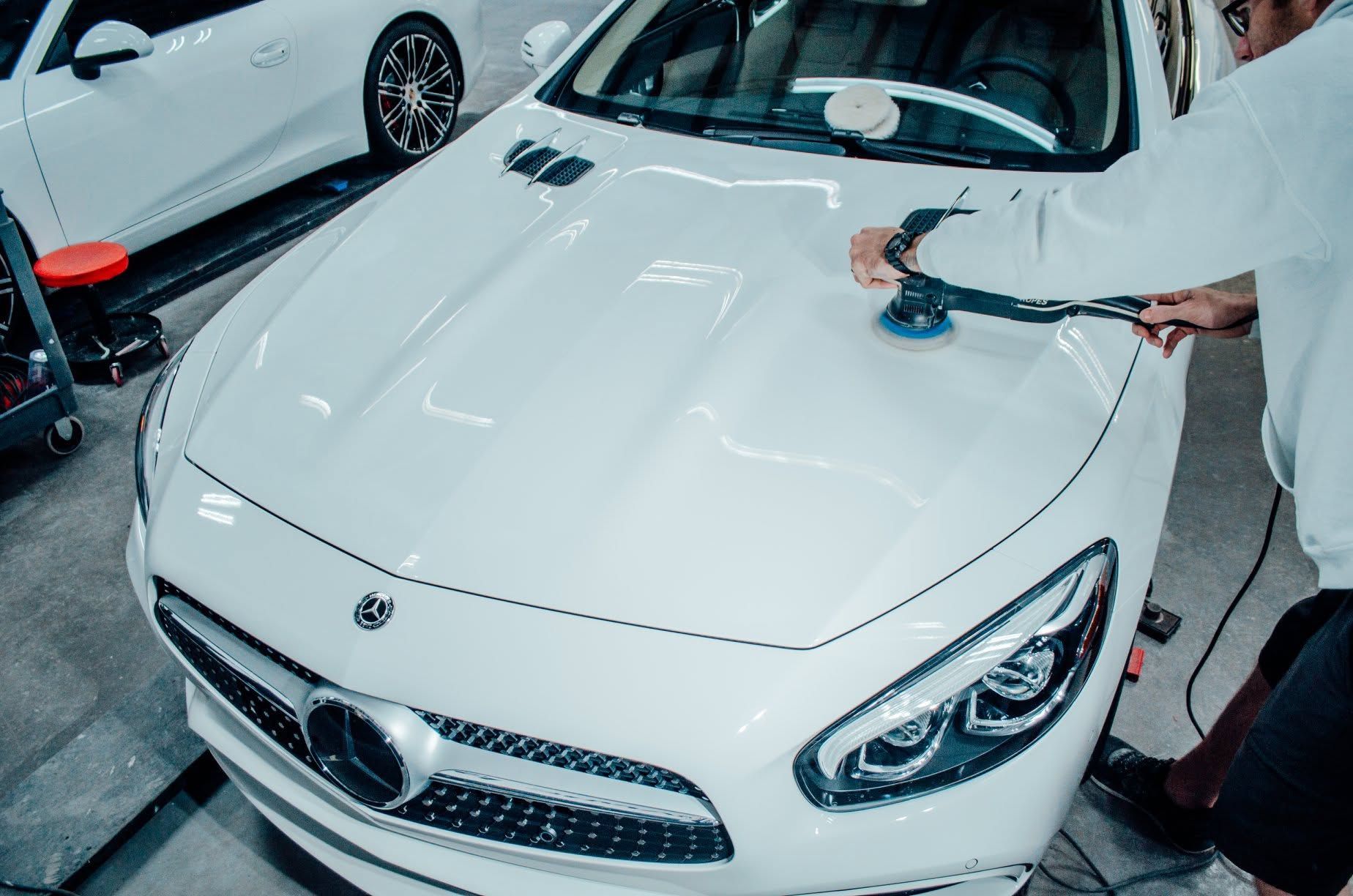 Person polishing a white sports car in a garage, with another car nearby