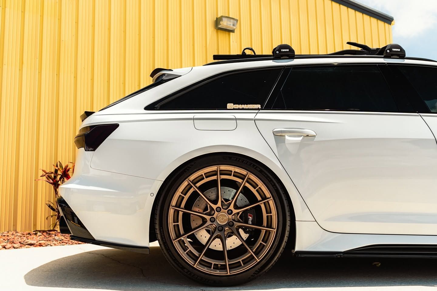 White lowered station wagon with bronze wheels parked beside a yellow corrugated wall