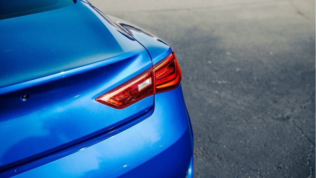 Rear view of a blue car on pavement, showing the taillight and trunk corner