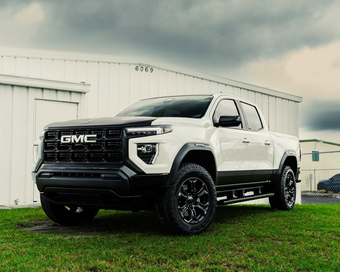 White GMC pickup truck parked on grass beside a white building under cloudy skies